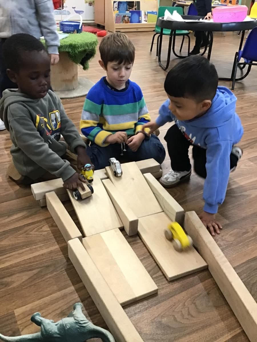 three children play with toy cars on a wooden ramp track at destiny haven nurser